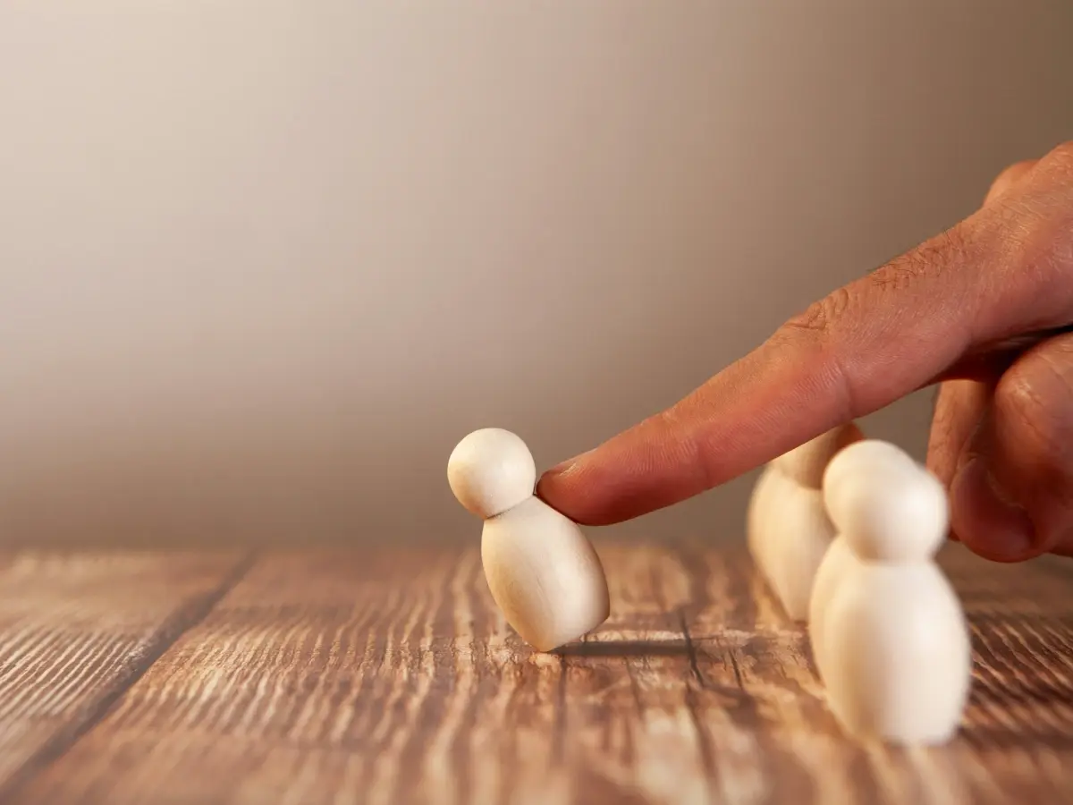 A finger singles out one wooden figure from a small group on a wooden table
